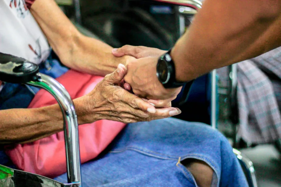 Man holding hand of elderly woman on a chair stock photo